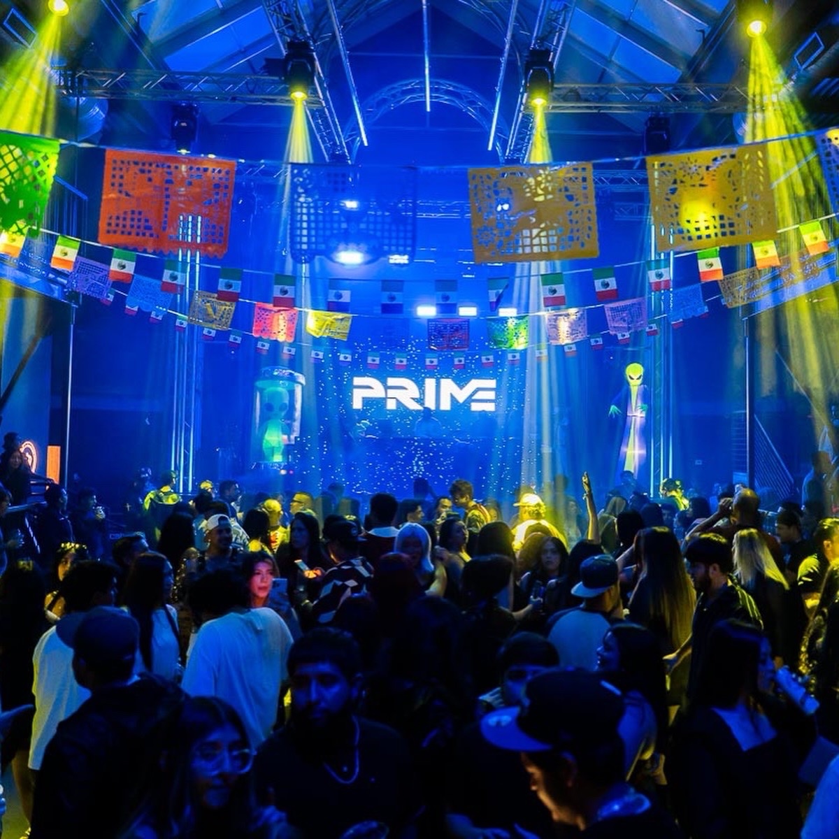 A packed dance floor under blue and yellow lighting with PRIME on the stage screen.